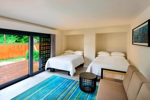 two beds in a room with a couch and a patio at Sheraton Resort & Spa, Tokoriki Island, Fiji in Tokoriki