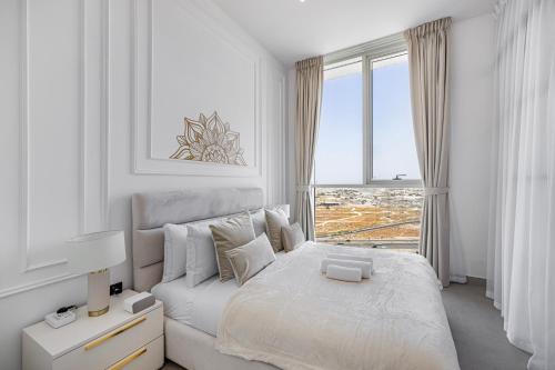 a white bedroom with a bed and a large window at Luxury Apt in Dubai Hills Burj Khalifa views in Dubai