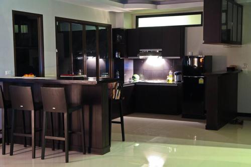 a kitchen with black cabinets and a bar with stools at Serenity Shores - 2 King Bed - Beachfront Penthouse in Plai Laem