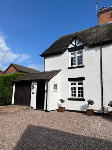 a white house with a garage and two plants at One Jubilee Cottages in Shugborough