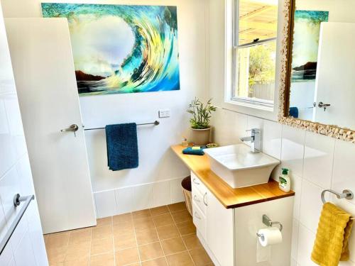 La salle de bains est pourvue d'un lavabo et d'une peinture murale. dans l'établissement Yamba Fishing Cottage Haven Wifi boat parking, à Yamba