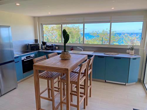 a kitchen with blue cabinets and a wooden table with chairs at Appartement Happy View - Vue mer paradisiaque - Jacuzzi in Friar's Bay