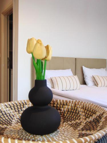 a black vase with flowers on a table next to a bed at Apartmani L in Novi Pazar
