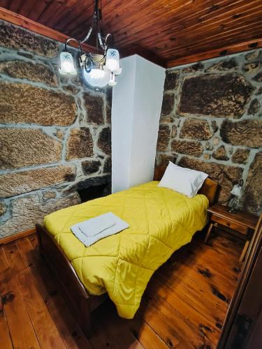 a bedroom with a yellow bed in a stone wall at Quinta das Amendoeiras in Meda