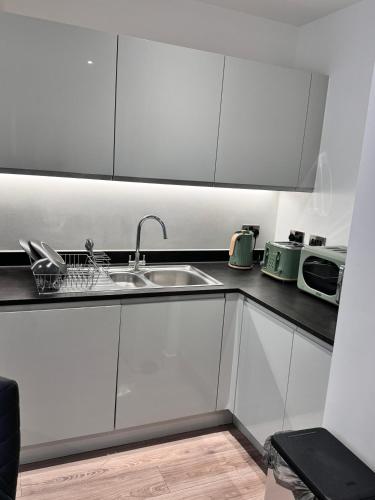 a kitchen with white cabinets and a sink at Stylish Luxury Solihull Flat in Olton