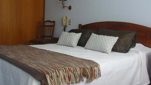 Una cama con sábanas blancas y almohadas. en Hotel Chalet Suizo, en Viña del Mar