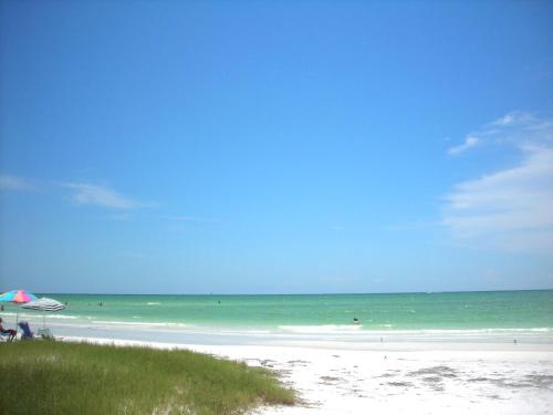 a beach with people sitting under an umbrella and the ocean at Newly remodeled 8-steps to sand path of Beach! in Siesta Key