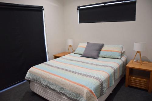 a bedroom with a bed with a striped blanket and two tables at Seven On Myrtle at Hat Head - Bring your own linen. in Hat Head