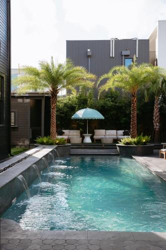 a swimming pool with palm trees and an umbrella at Blackbird Hotel in New Orleans