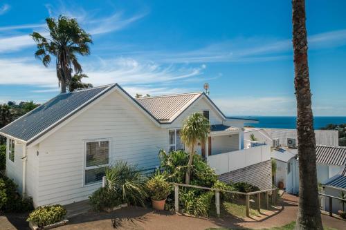 a white house with palm trees and the ocean in the background at Palm Beach Penthouse by Waiheke Pure in Palm Beach