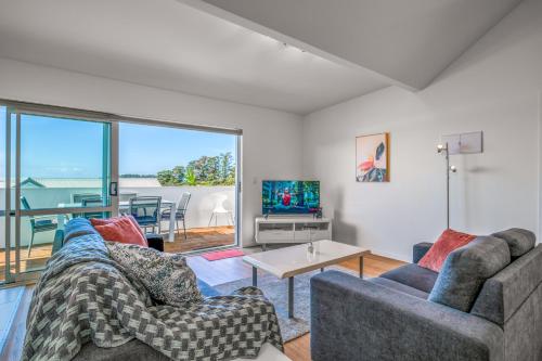 a living room with two couches and a tv at Palm Beach Penthouse by Waiheke Pure in Palm Beach