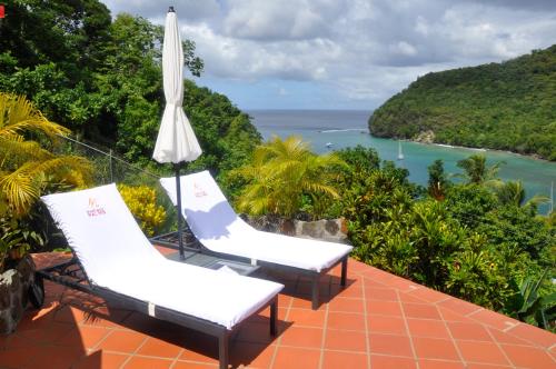 two lounge chairs and an umbrella on a balcony overlooking the ocean at Marigot Palms Luxury Caribbean Apartment Suites in Marigot Bay