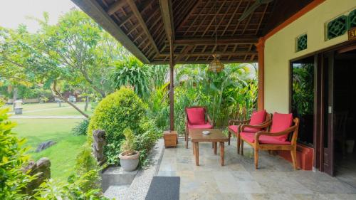 a porch with two red chairs and a table at Taman Sari Bali Resort and Spa in Pemuteran