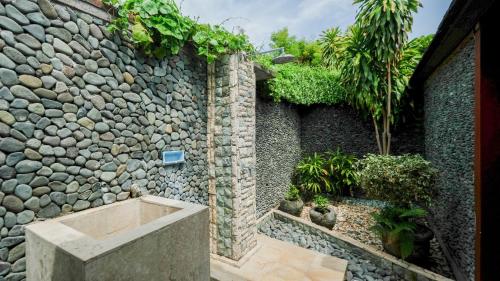 a bathroom with a stone wall and a bath tub at Taman Sari Bali Resort and Spa in Pemuteran