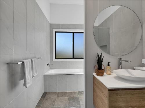 a white bathroom with a sink and a mirror at Chic 4-Bed with 3 Living Areas & Alfresco Dining in Malua Bay