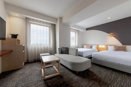 a hotel room with two beds and a chair at Hotel Vista Kanazawa in Kanazawa