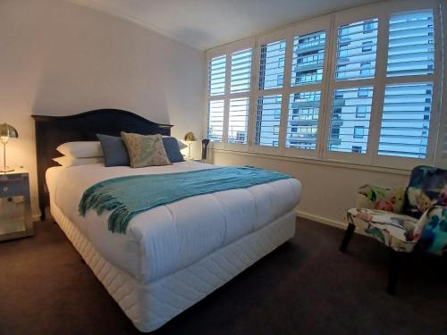 a bedroom with a bed and a chair and windows at ReadySet Apartments at Southbank Condos in Melbourne