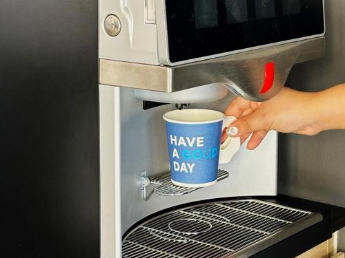 a person is putting a cup into a coffee maker at HOP INN Prachuap Khiri Khan in Prachuap Khiri Khan