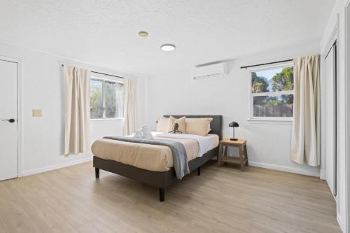 a white bedroom with a bed and two windows at # Marbella Lane - Modern Cabin-style 2BR Home in Campbell