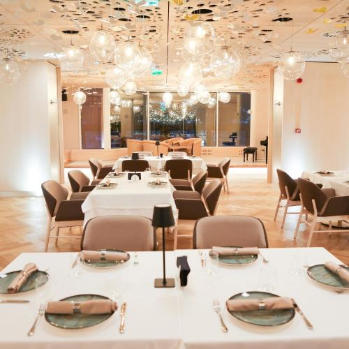 a restaurant with white tables and chairs and chandeliers at Hotel Aro Palace in Braşov
