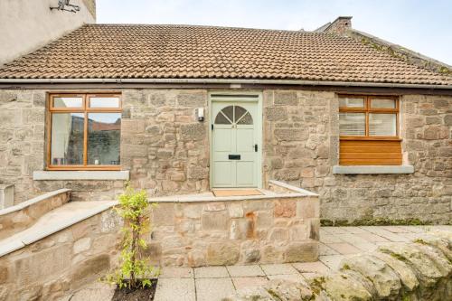 a stone house with a green door and windows at Harrow Bank Cottage Family and Pet Friendly Coastal Escape in Tweedmouth in Tweedmouth