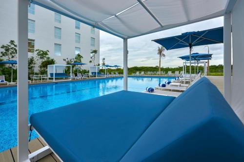 a large swimming pool with a blue table and umbrellas at City Express Plus by Marriott Cancun Aeropuerto Riviera in Cancún