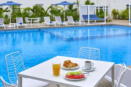 a table with fruit and juice next to a swimming pool at City Express Plus by Marriott Cancun Aeropuerto Riviera in Cancún