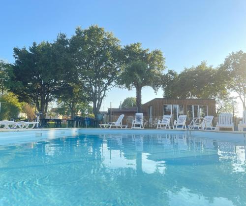 une grande piscine avec des chaises blanches et des arbres dans l'établissement Chalet Camping du grand fay, à Saint-Père-en-Retz