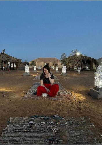 a woman sitting on the ground in a field at Aladdin merzouga camp in Merzouga