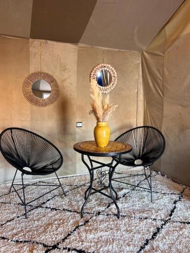 two chairs and a table with a vase on it at Aladdin merzouga camp in Merzouga