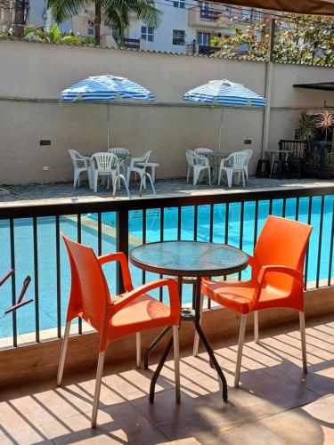 a table and chairs next to a swimming pool at Pousada Parque Suites - Estacionamento e Piscina in Guarujá
