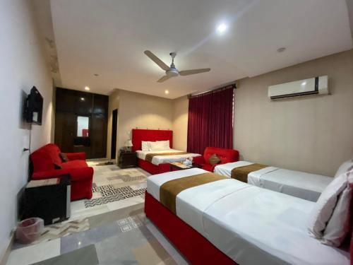 a bedroom with two beds and a red chair and couch at Hotel Tulip Inn, Gulberg in Lahore