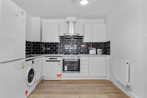 a kitchen with white cabinets and a washer and dryer at Spacious Sleep 14 - 1 min from Tooting Station MR3 in London
