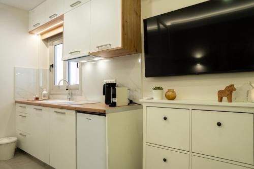 a kitchen with white cabinets and a flat screen tv at Armonía Luxury Apartments in Ierápetra