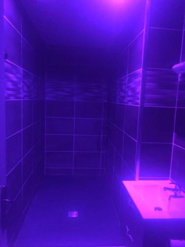 La salle de bains est pourvue d'un lavabo et d'une lumière violette. dans l'établissement L appartement soleil de willerval, à Willerval