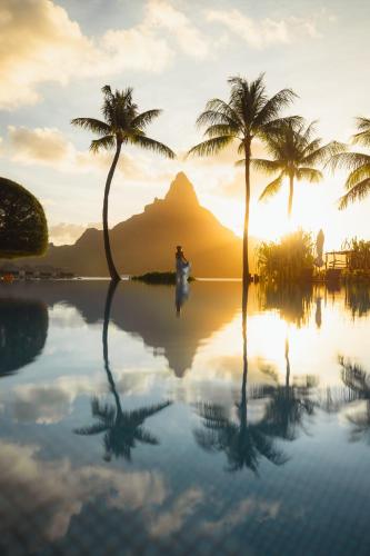 a man standing in a infinity pool with palm trees at InterContinental Bora Bora & Thalasso Spa by IHG in Bora Bora