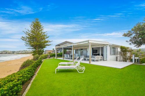 a house with a bench on the lawn next to the beach at Wamberal Beach(shares with Terrigal Beach)Terrigal Beach SummerBelle Beachfront House in Wamberal