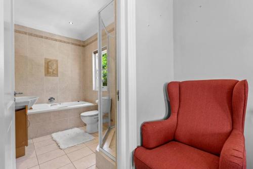 a red chair in a bathroom with a tub and a toilet at SunsetViews Houtbay in Hout Bay
