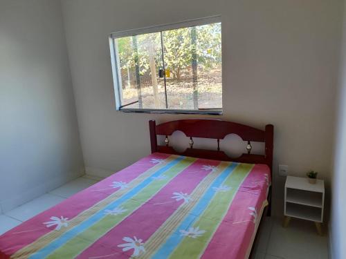 a bedroom with a bed with a colorful comforter and a window at Casa espaçosa em frente à pracinha in Capitólio