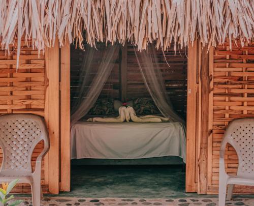 a bed in a wooden cabin with two chairs at Magic Green Dentro del Parque Tayrona in El Zaino