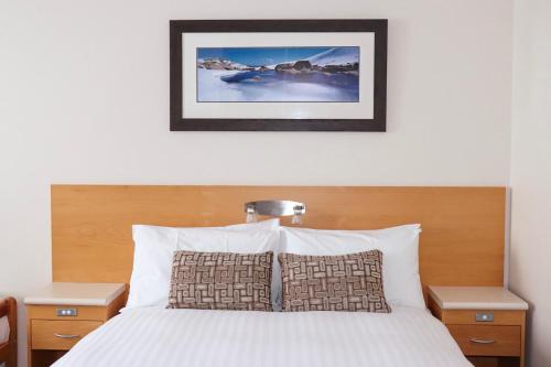 a bedroom with a bed with white sheets and a picture on the wall at Smiggins Hotel & Chalet Apartments in Perisher Valley
