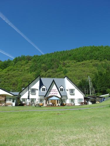 a large white building in front of a grass field at Pension Kaoru in Kiso