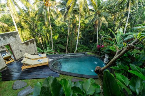 a swimming pool in the middle of a garden with palm trees at Madani Antique Villas in Ubud