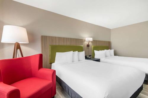 a hotel room with two beds and a red chair at Country Inn & Suites by Radisson, Atlanta Airport South, GA in Atlanta