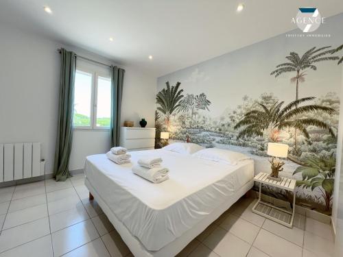 - une chambre avec un grand lit blanc et des palmiers sur le mur dans l'établissement Villa Jade, à Grimaud