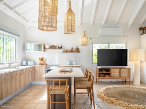 a kitchen with a table with chairs and a tv at Be Happy à pied de Friar's Bay face au coucher de soleil in Friar's Bay
