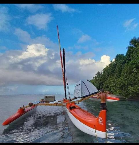 a man is standing next to a boat in the water at Bungalow climatisé chez Kim in Taputapuapea