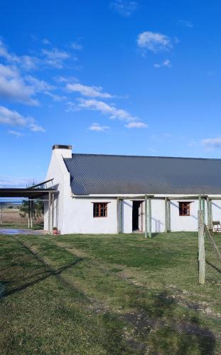 a white building with a black roof on a field at Barn Owl Cottage in Riethuiskraal