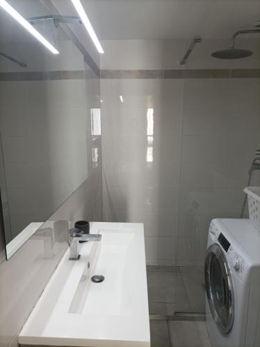 une salle de bain blanche avec une machine à laver et un lavabo dans l'établissement Agréable Appartement Proche Plage - Linge de lit et Toilettes en option, à La Grande Motte
