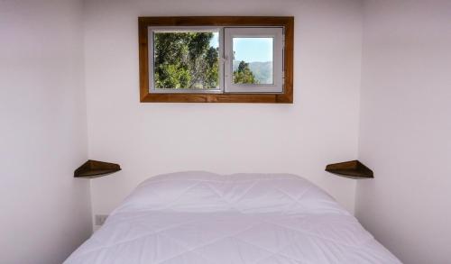 a bedroom with a white bed with a window at Refugio del Hornero Norte in San Carlos de Bariloche